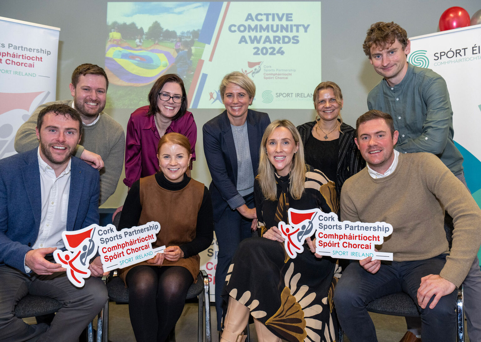 Staff of Cork Sports Partnership sitting in front of sign for Active Community Awards.