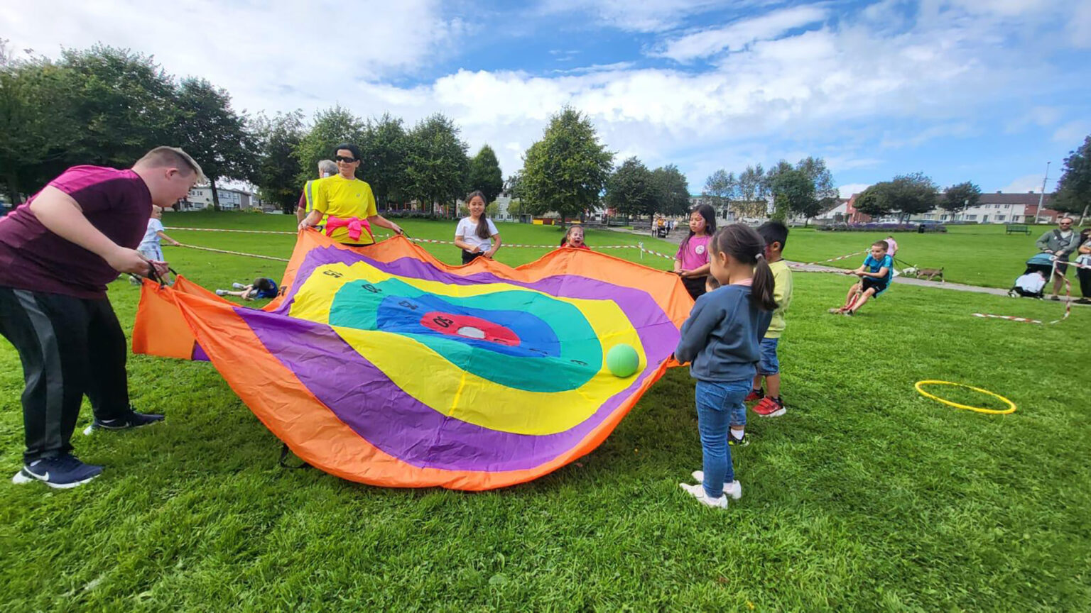 Group of kids and adults playing in park on a sunny day.